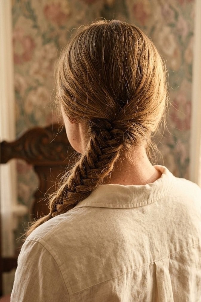 Loosened fishtail braid pulled over one shoulder, honey brown textured hair seen from behind