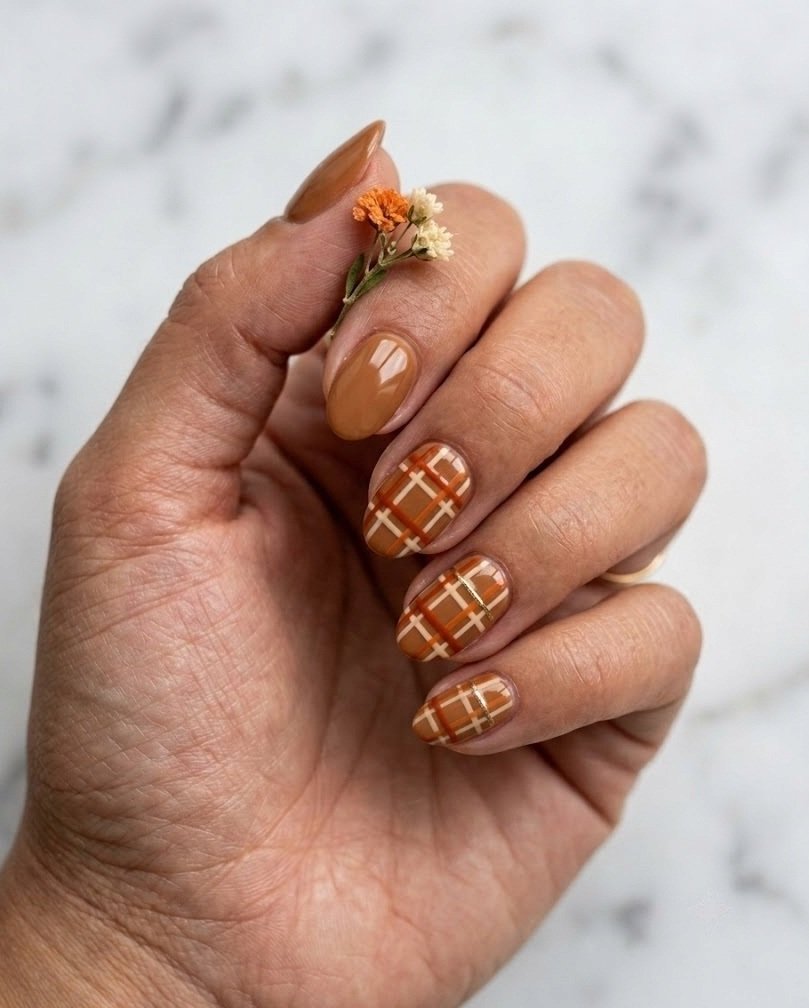 Short almond nails with caramel base and burnt orange and cream plaid grid on two nails