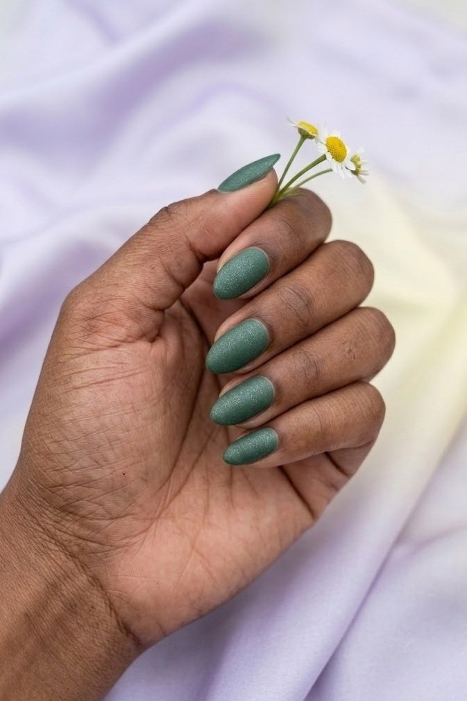 Matte pine green short almond nails with a fine silver micro-shimmer like frost.