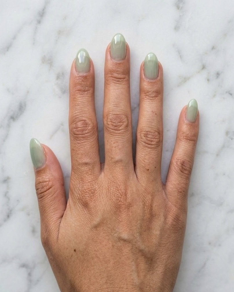 Short almond nails in sheer milky sage green on a medium skin tone hand