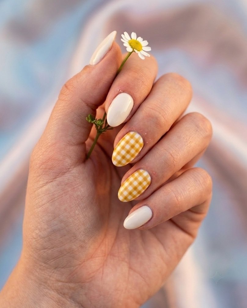 Short almond nails with small mustard gingham squares on a cream base