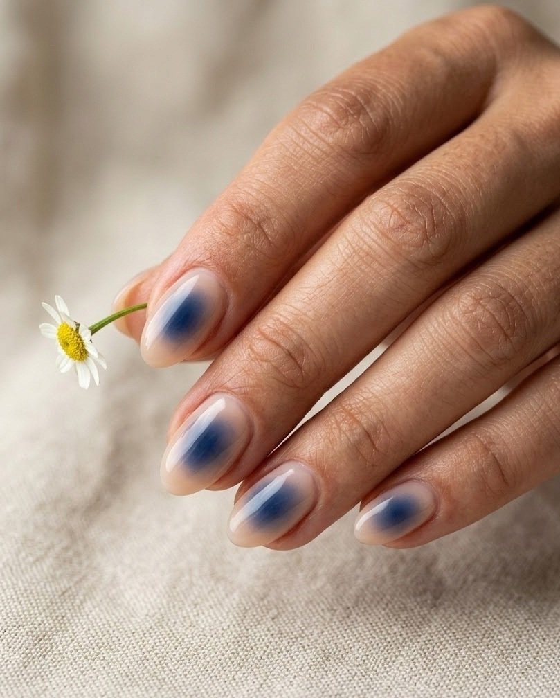 Sheer nude short almond nails with a soft navy aura glowing from the center on beige linen