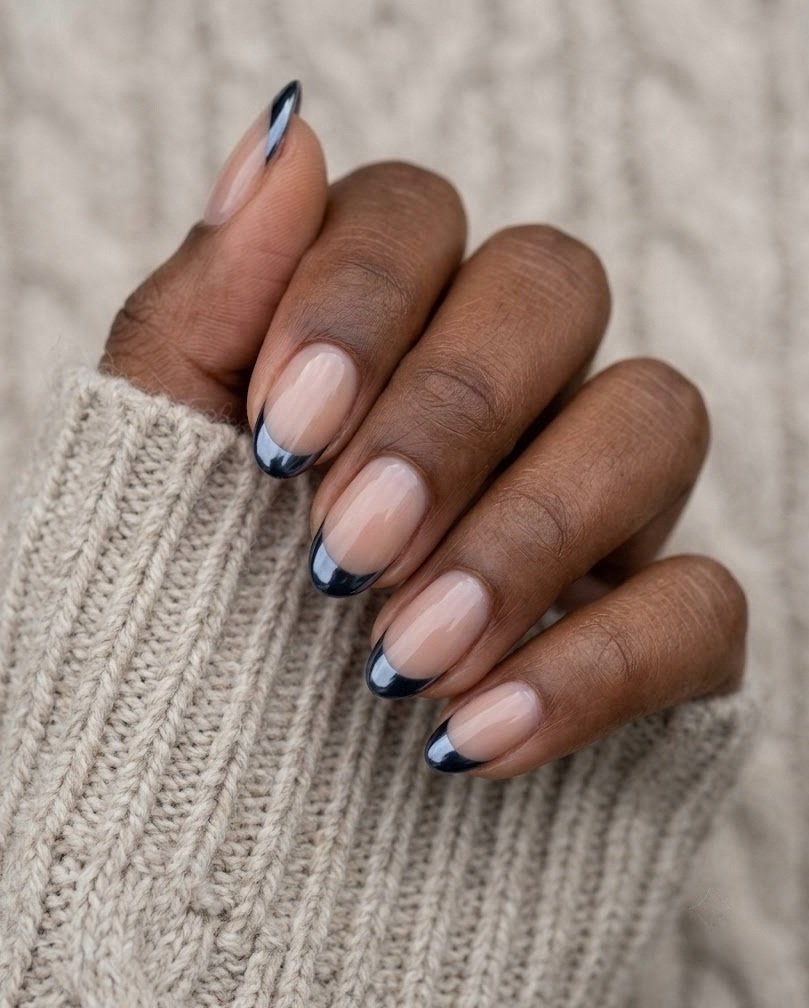 Sheer nude short almond nails with a thin navy chrome French tip on a knit sweater sleeve