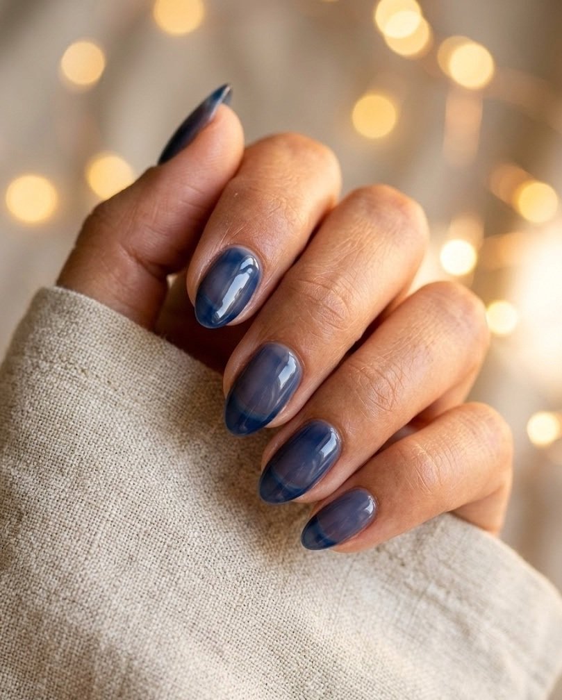 Sheer translucent navy glass short almond nails glowing against blurred fairy lights