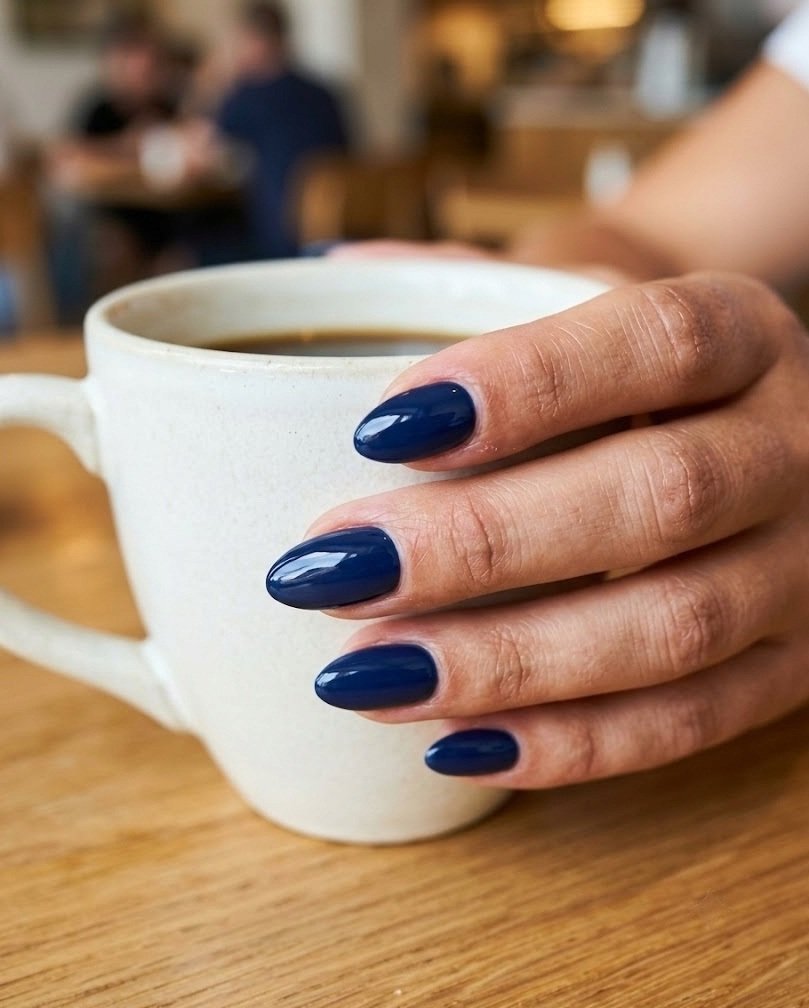 Solid deep glossy navy short almond nails on a wooden cafe table