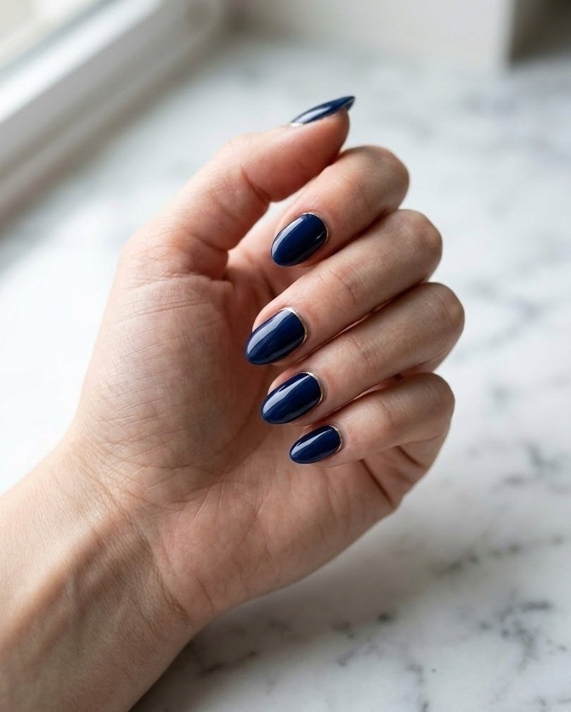 Glossy navy short almond nails with a thin gold line at the cuticle on white marble