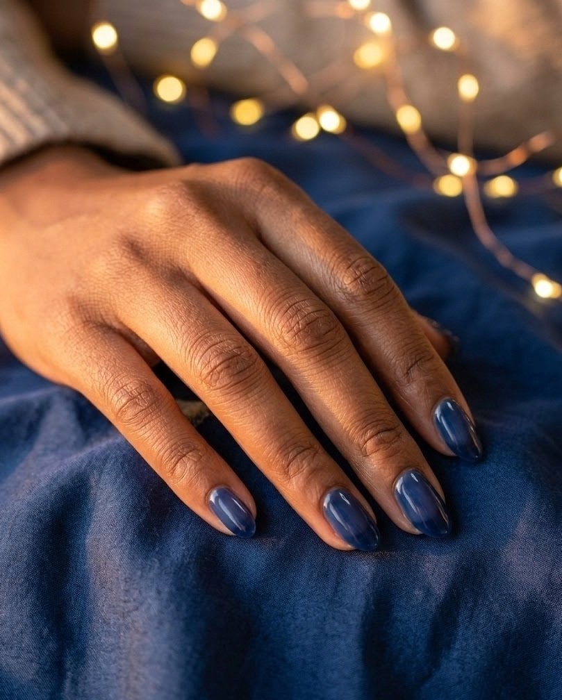 Sheer jelly navy short almond nails with a translucent candy finish against fairy lights