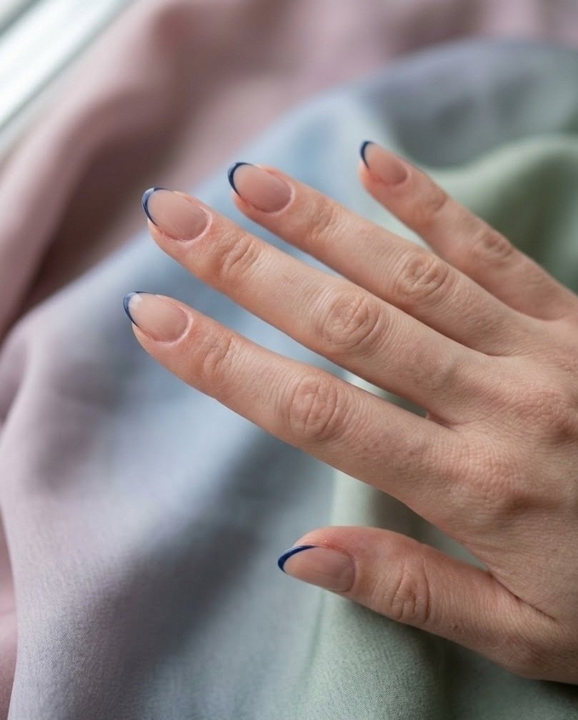 Sheer nude short almond nails with a very thin navy micro French line on pastel silk