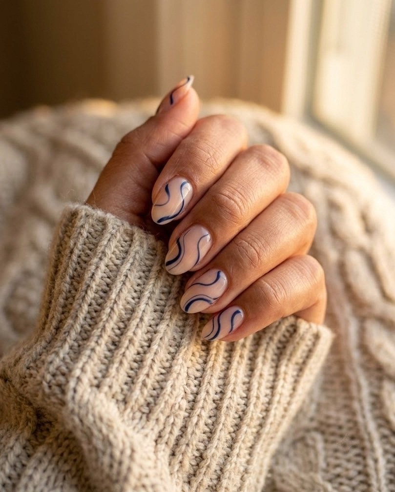 Bare short almond nails with thin navy swirls and negative space on a knit sweater sleeve