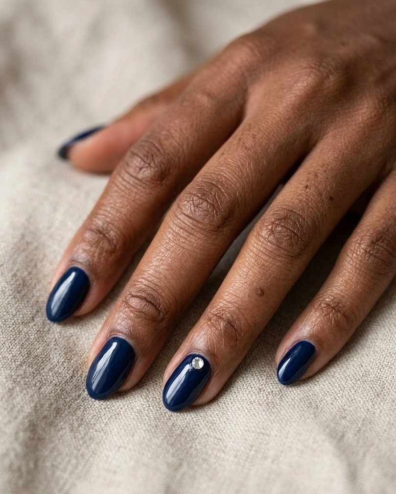 Glossy navy short almond nails with one small gem near the cuticle on beige linen