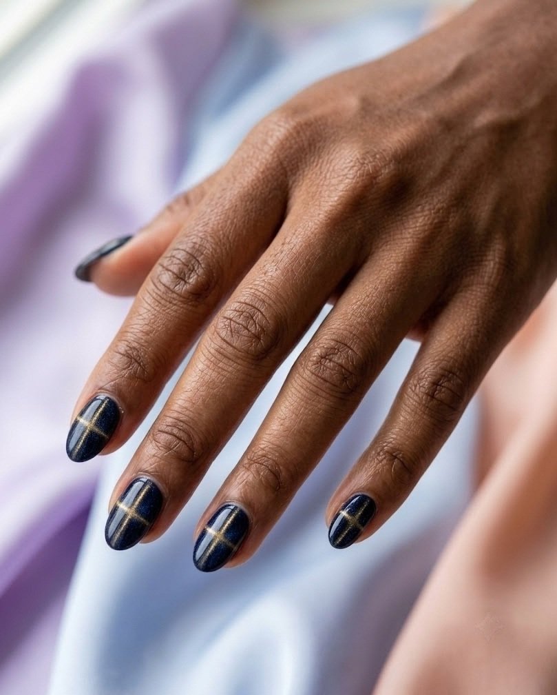 Deep navy velvet short almond nails with a thin gold cross of light on pastel silk