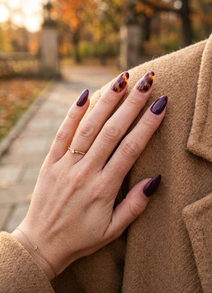 Tortoiseshell accent nails paired with solid dark plum almond nails