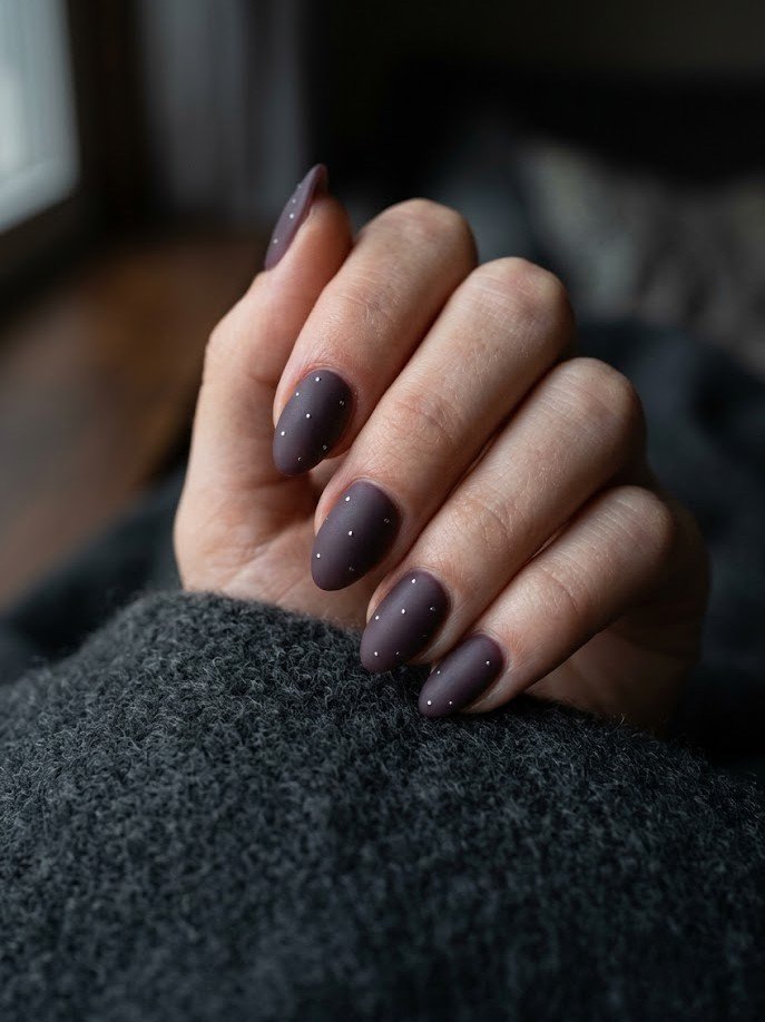 Matte smoky plum nails with tiny metallic dots on short almond shape