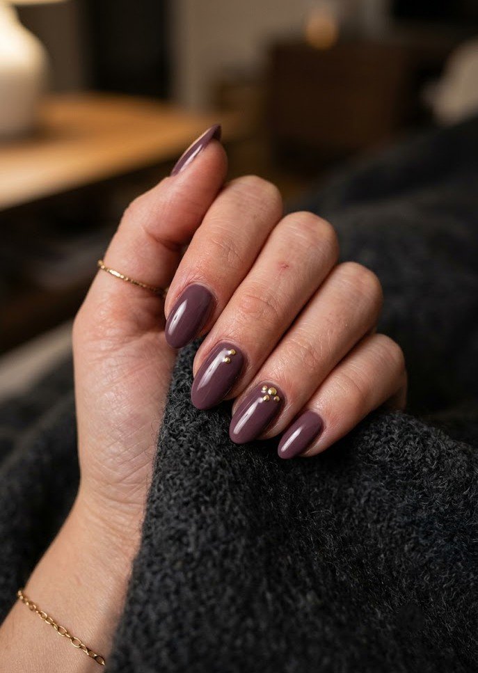 Glossy smoky plum nails with small gold studs on short almond shape
