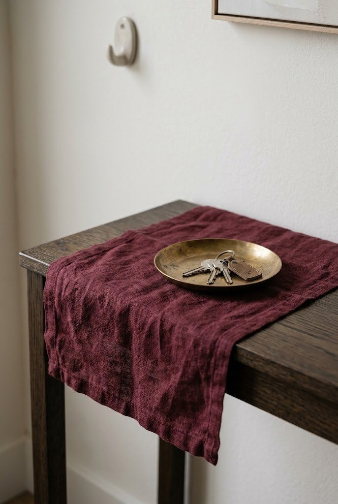 Burgundy linen table runner on a slim console with a small brass dish on top