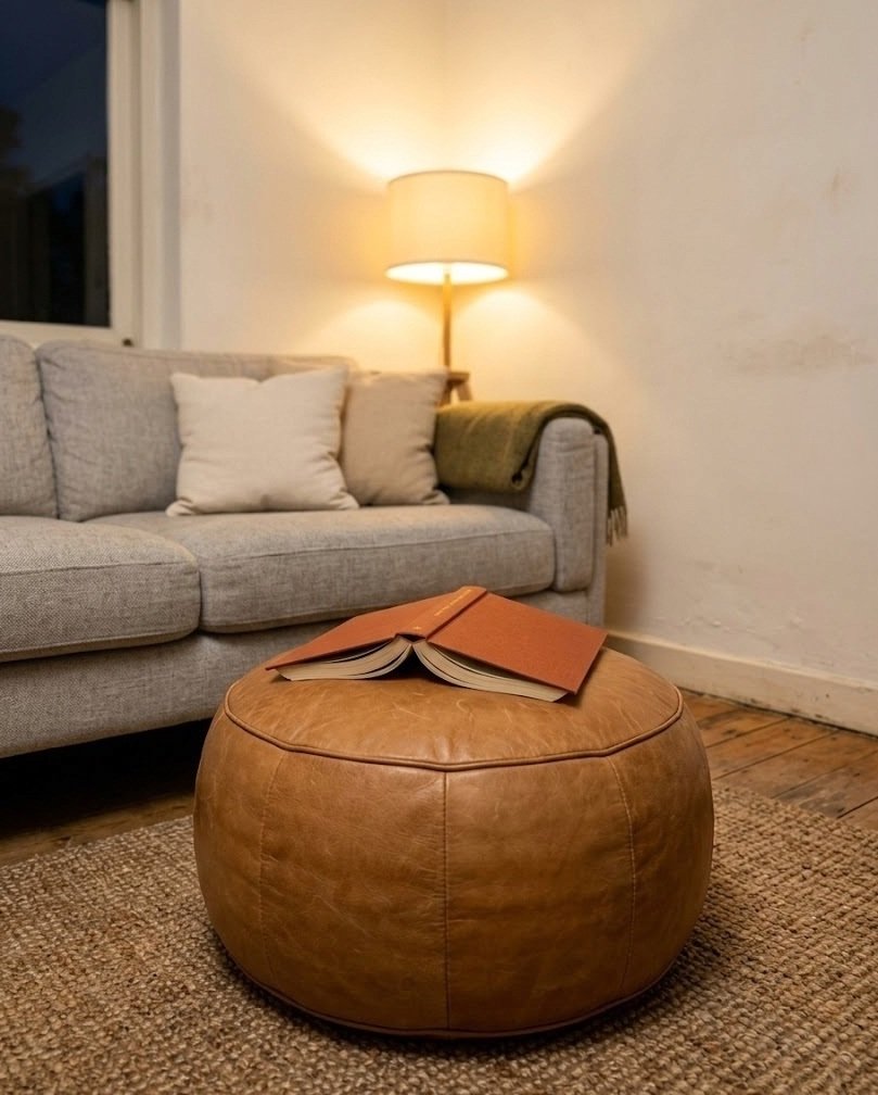 Round caramel tan leather pouf on a jute rug in front of a neutral sofa