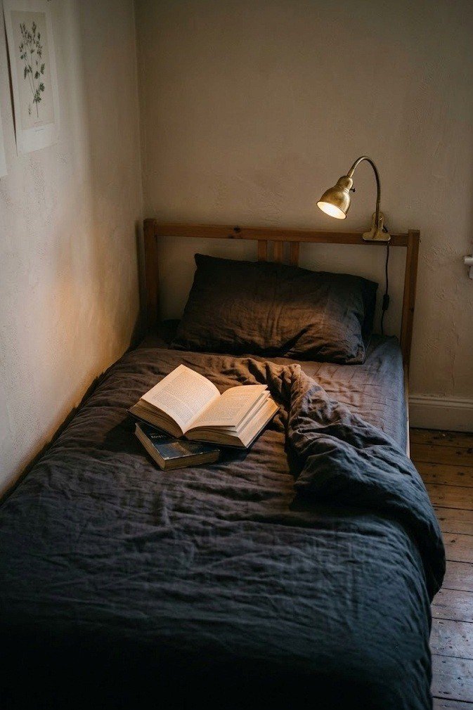 Small brass clip on reading light clamped to a wooden bed frame with its beam angled onto an open book on the bedding