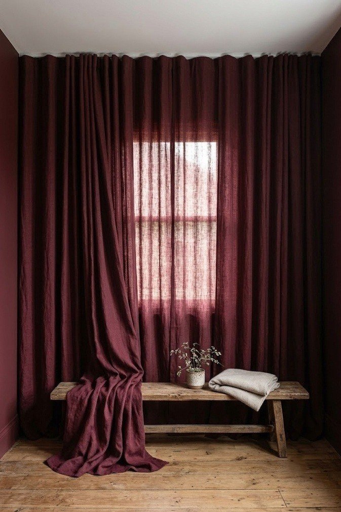Floor length deep burgundy linen drapes on a ceiling mounted track covering a full wall and its single window in a small bedroom