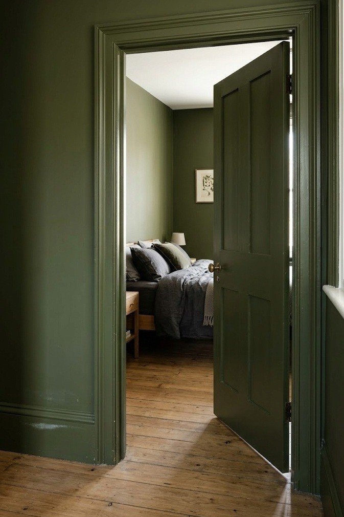 Bedroom doorway with the baseboard, door frame and door painted the same deep olive green as the matte walls