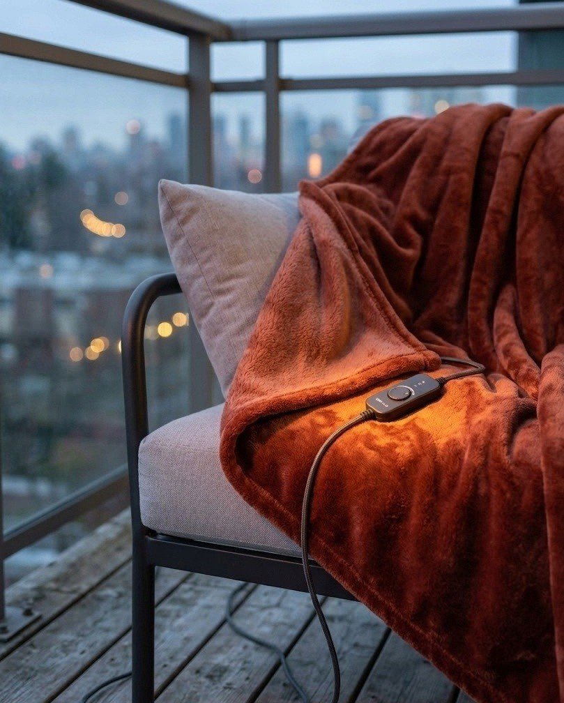 Deep rust heated throw blanket draped over a balcony lounge chair