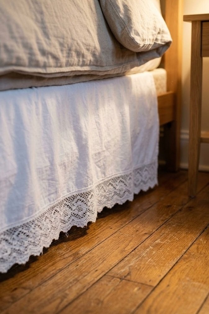 white bed skirt with a lace hem peeking below a neutral duvet on a wood floor