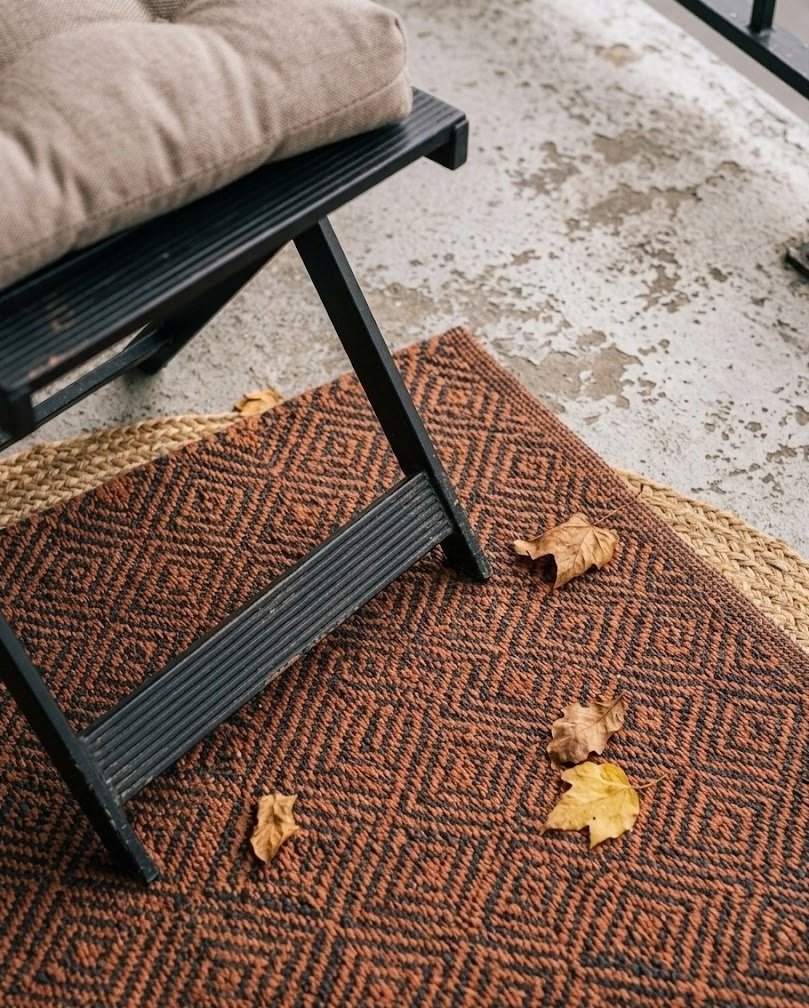 Warm rust and charcoal diamond outdoor rug on a balcony concrete floor
