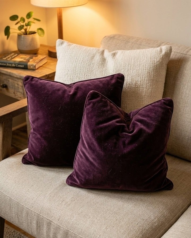 Two deep plum velvet lumbar pillows propped against cream cushions on a neutral sofa