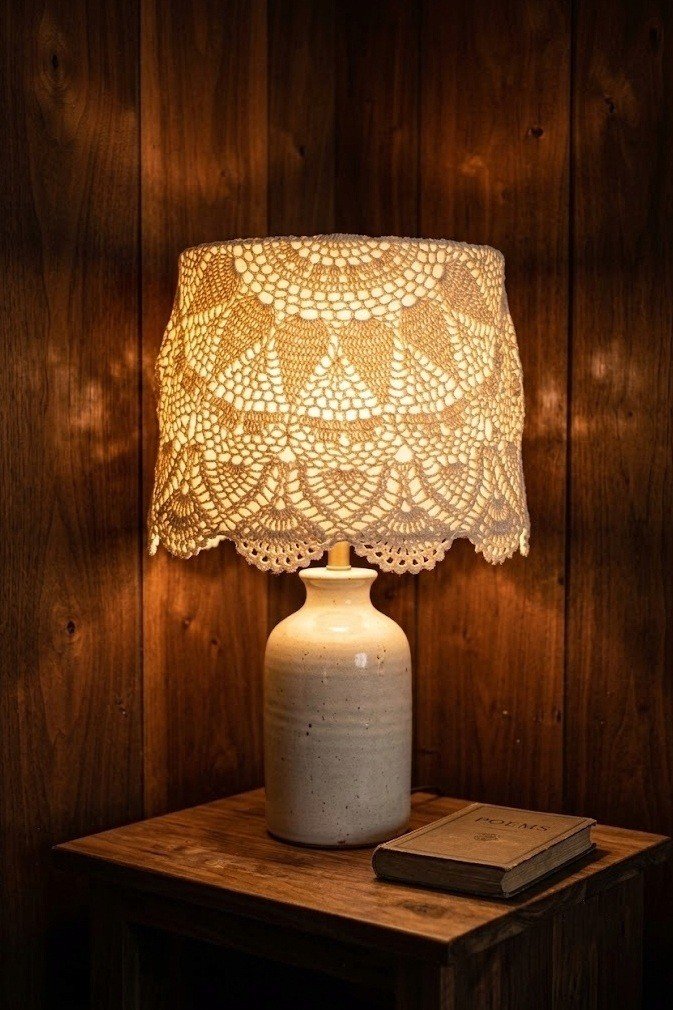 cream doily laid over a drum lampshade on a glowing ceramic table lamp