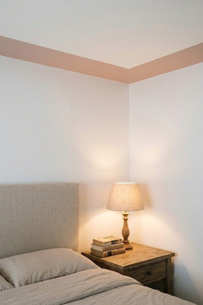 A single soft clay horizontal band framing the perimeter edge of a small bedroom ceiling