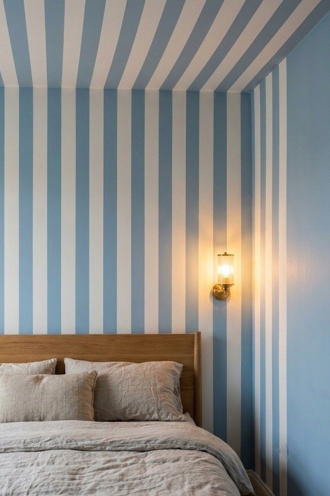 Soft blue and white vertical stripes wrapping from the headboard wall over the ceiling line