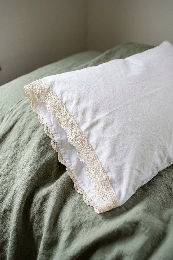 white cotton pillowcase with a narrow vintage crochet lace trim on sage green linen